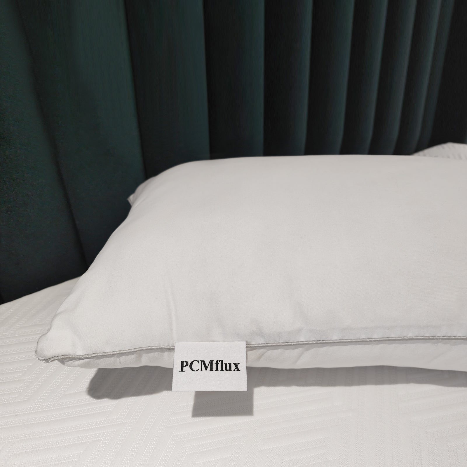 PCMflux white pillow with gray stitching on textured white bedspread, against a dark green tufted headboard.