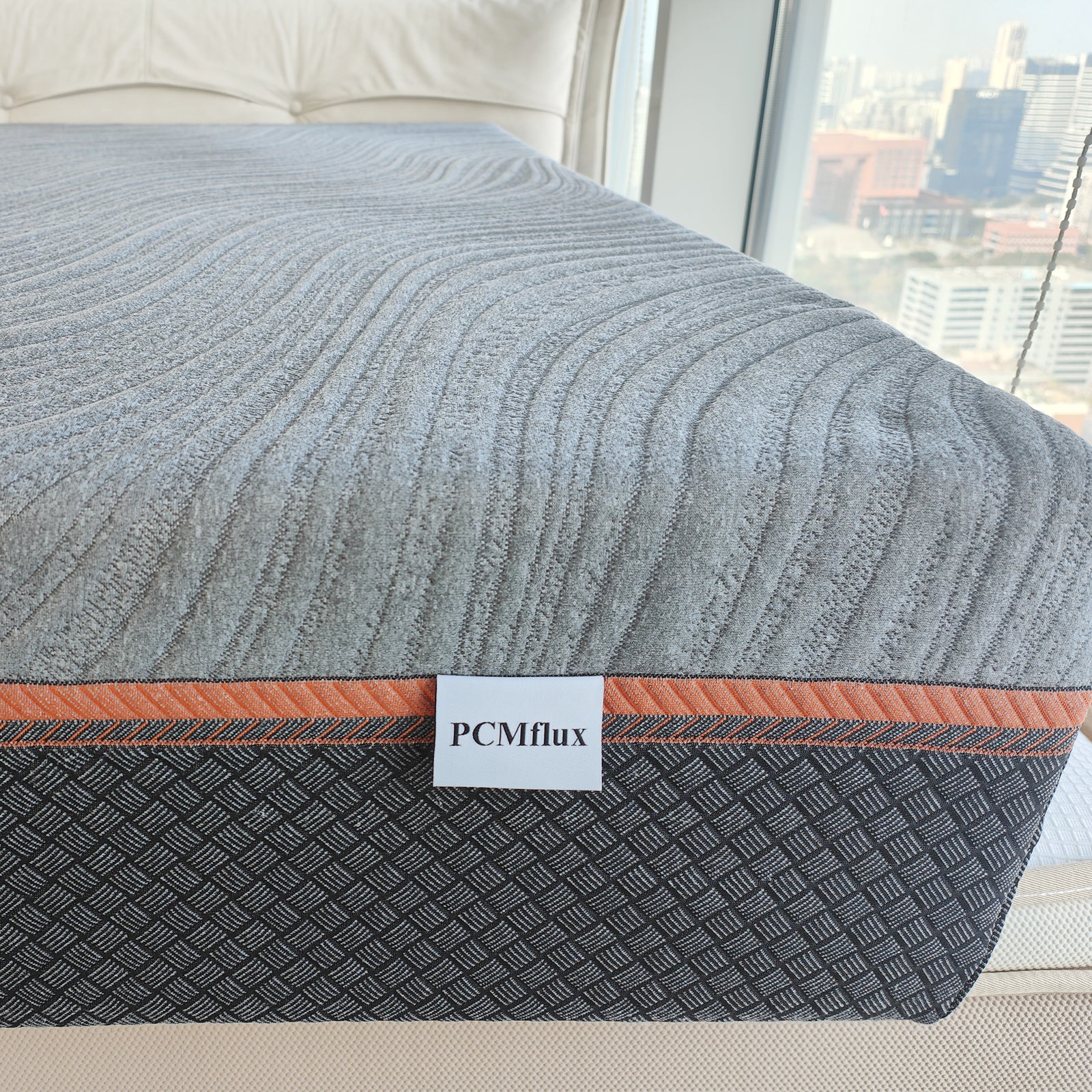 PCMflux Memory Foam Mattress with wavy grey top, orange stripe, and basketweave dark grey base. Reversible design.