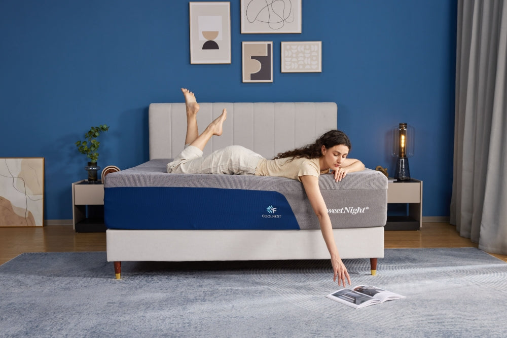 A woman is relaxing on a SweetNight CoolNest gel memory foam mattress in a stylish blue bedroom, reaching down towards a magazine.