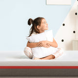 Child smiling while sitting on a mattress, holding a pillow, showcasing comfort for Best Mattress Brands.