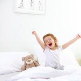 Child joyfully waking up in bed with a teddy bear, showcasing comfort of SweetNight CoolNest Mattress.