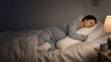 Pregnant woman asleep on her side hugging a body pillow in a calm, dimly lit bedroom