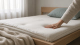 Hand pressing into a bare mattress surface showing a soft depression, illustrating a mattress losing support over time