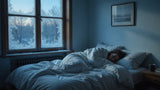 Person sleeping snugly in a cold bedroom with a frosted window in cool morning light