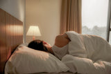 woman sleeping on the side with her back turned on a white pillow underneath a white blanket