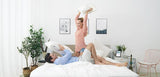 Couple playfully having a pillow fight on a bed, showcasing comfort of All Products collection with cooling and hybrid mattresses.
