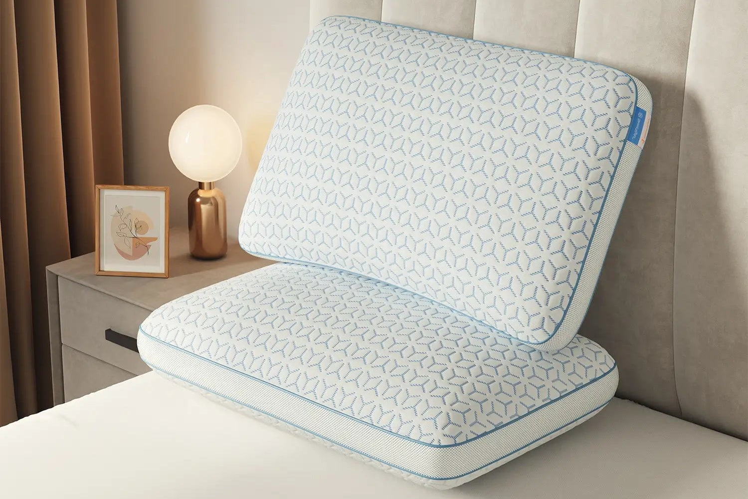 Blue and white pillow on a bed with a nightstand and lamp in the background